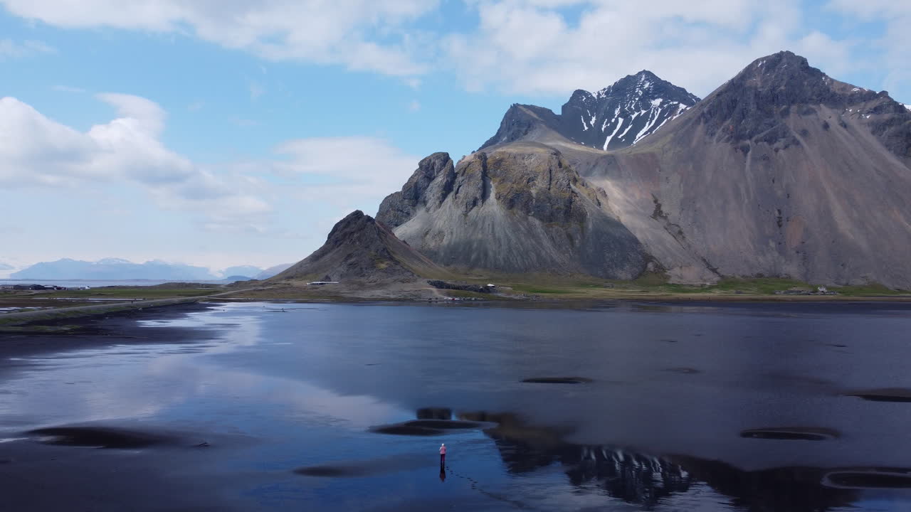 검은 해변의 물에 반사된 산을 경외하며 걷는 사람