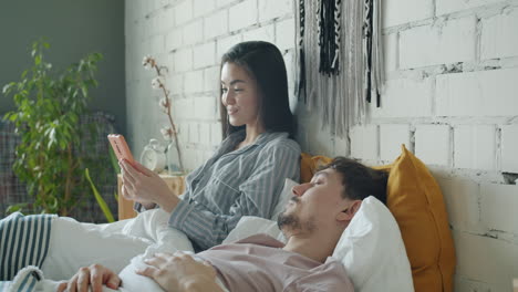 couple relaxing in bed, woman looking at phone
