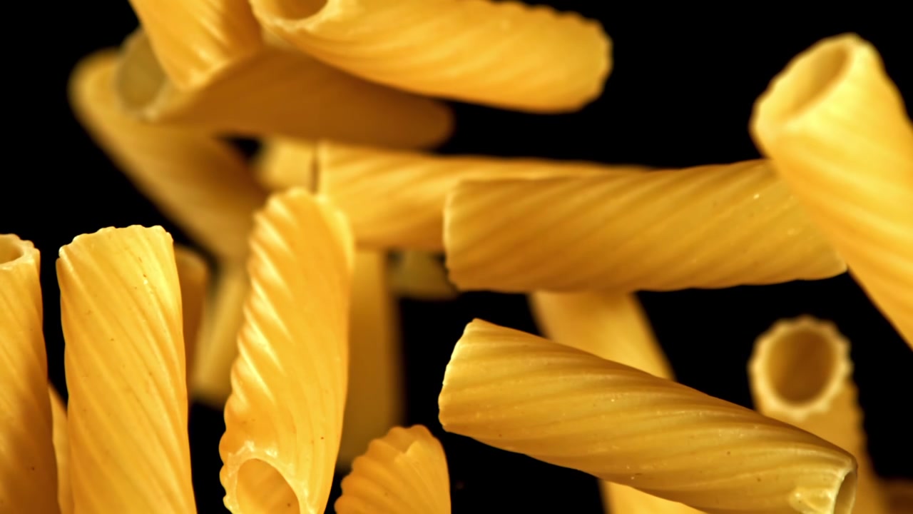 Tubetti di pasta secca dorati che cadono su sfondo nero