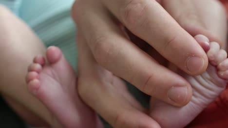adult hand and fingers holding tiny newborn baby feet - close up
