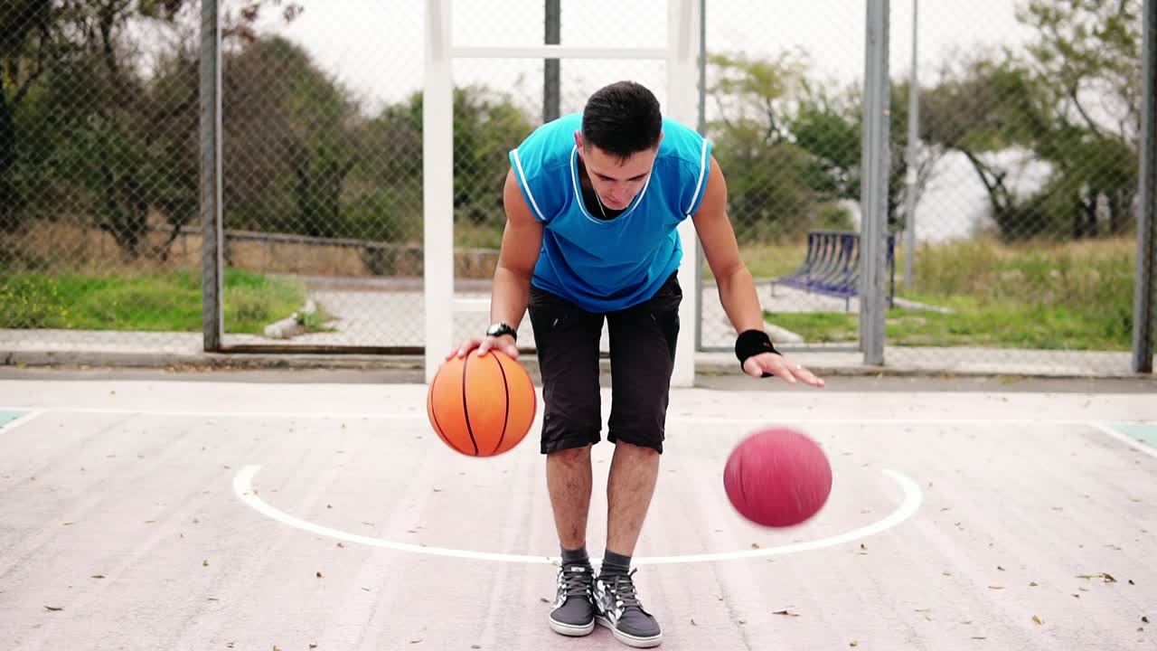 vista de cerca de un joven practicando baloncesto en la cancha de la calle. está jugando con dos pelotas simultáneamente. cámara lenta