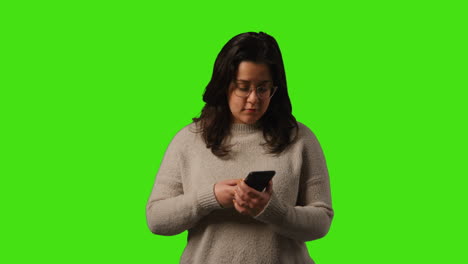 young woman getting alert and looking at text message on mobile phone standing against green screen background