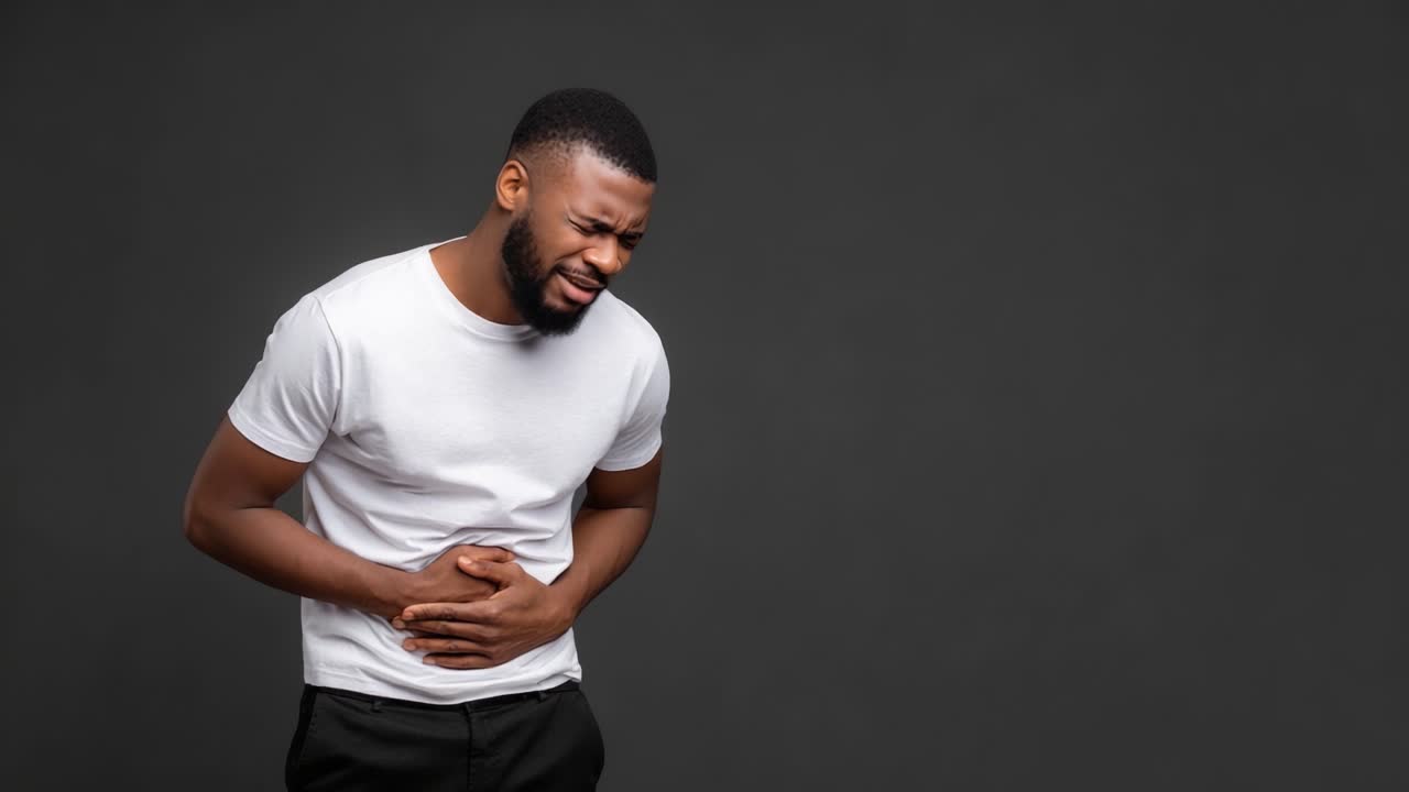 Un uomo mostra un disagio visibile mentre prova dolore allo stomaco, evidenziando l'impatto del disturbo gastrointestinale su uno sfondo semplice