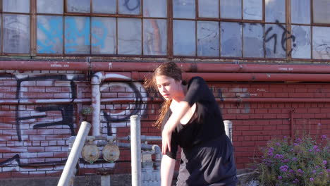 mujer blanca en cola de caballo bailando frente al almacén industrial