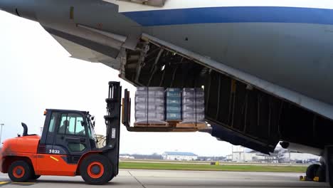 a forklift is unloading pallets of cargo from a large aircraft at the airport. the operation is efficient, showcasing the logistics of air transport and cargo handling.