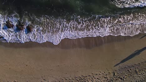 Aerial-view-of-beach-waves-with-a-couple-of-people-passing-by