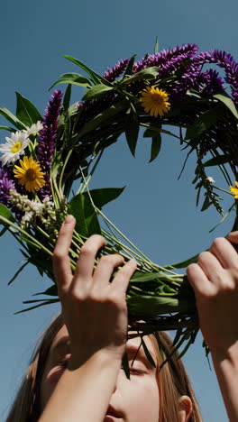 person holding a colorful flower wreath against a blue sky