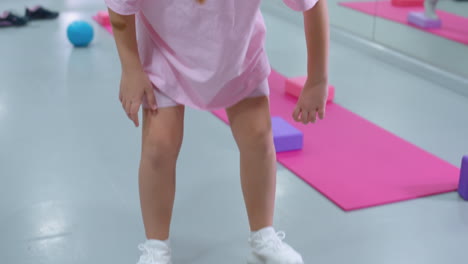 primer plano de un niño pequeño de color rosa equilibrando en una tabla, colocando una pelota de hierro en su lugar, rodeado de otros niños involucrados en actividades de fitness en un gimnasio