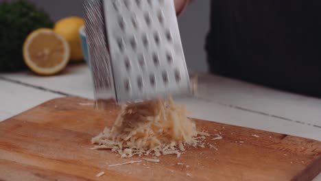 Grating-Parmesan-Cheese-On-A-Wooden-Board-Using-A-Surface-Glide-4-Sided-Box-Grater---tilt-down-shot