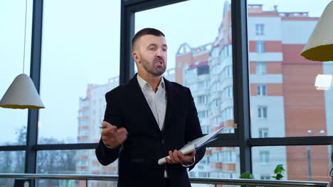 middle-aged boss in suit standing in front of employees and holding papers. man replying questions of his staff against city backdrop.