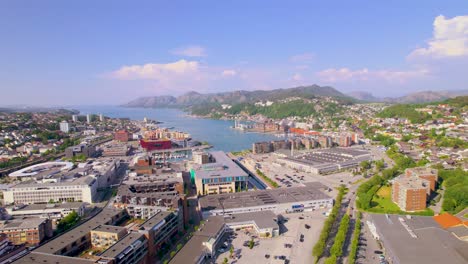 Drone-footage-of-a-City-at-the-end-of-a-Fjord-filled-with-blue-water,-mountains-and-nice-buildings