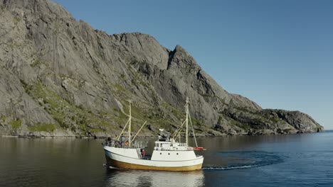 aerial drone shot of fishing boat on the ocean with huge rock faces and mountains in the background