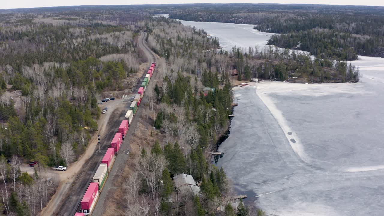 형형색색의 화물열차가 얼어붙은 호수를 따라 여행하면서 숲을 가로지른다
