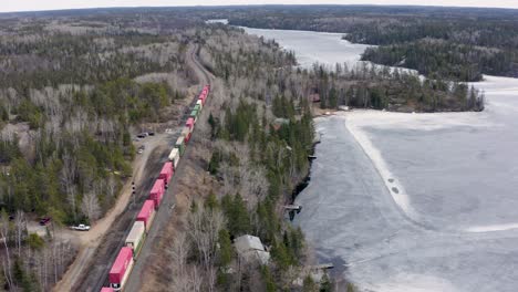 colorful freight train winds through the forest as it travels along side a frozen lake