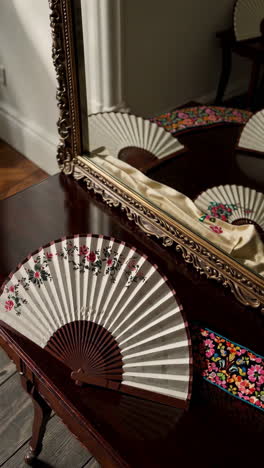 antique decorative fan on a wooden table in front of a mirror