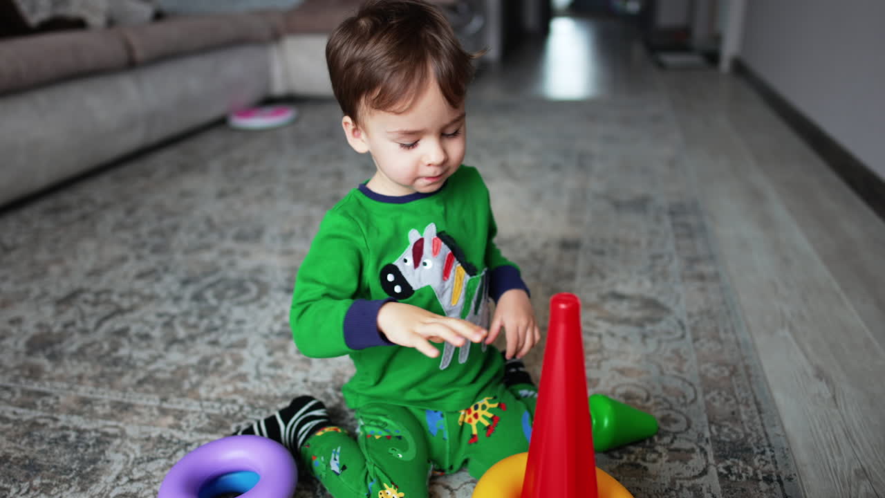 Beautiful toddler boy sitting on the floor assembles the pyramid. Lovely peaceful kid playing at home.