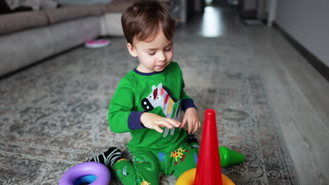 beautiful toddler boy sitting on the floor assembles the pyramid. lovely peaceful kid playing at home.