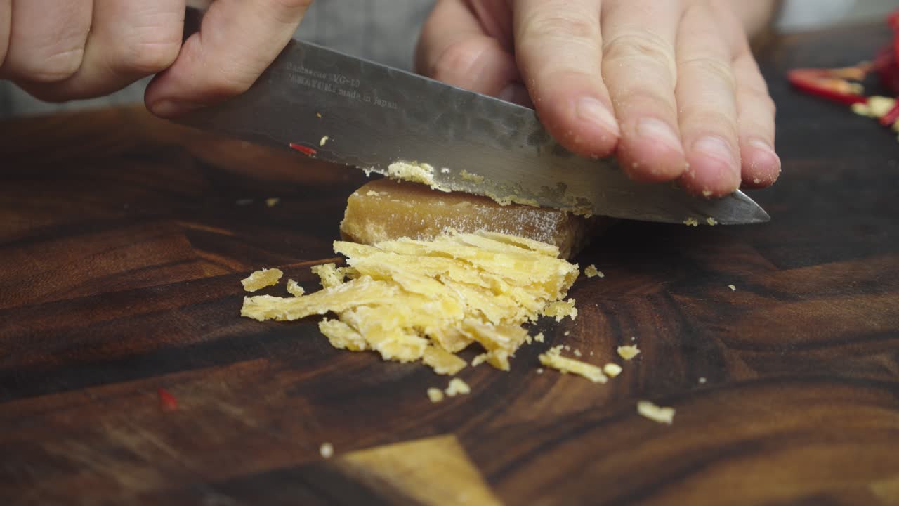 Chopping brown sugar with kitchen knife on wooden cut board
