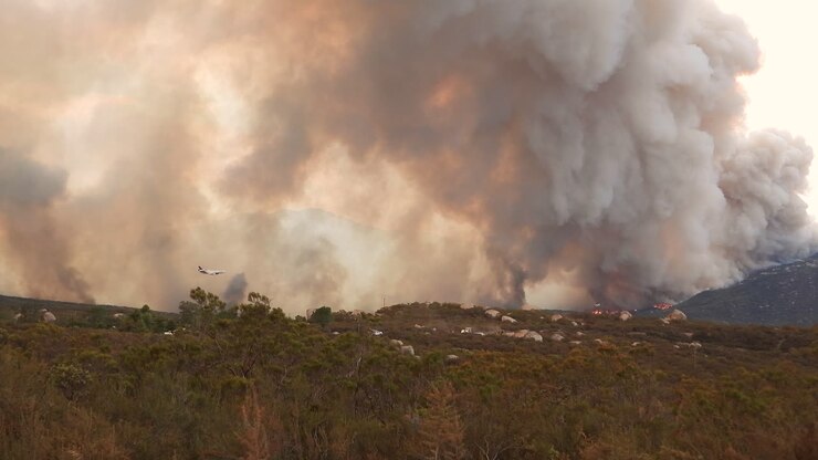 An Airtanker flying through bellowing smoke dropping a fire retardant red chemical Phos-Chek onto a fire in an attempt to contain the blaze during the Fairview wildfires, Hemet, California