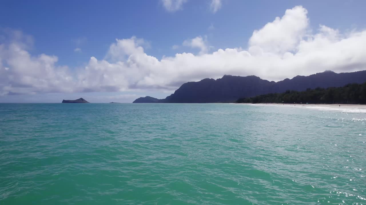 Aerial view of Waimānalo Beach’s vivid turquoise waters and tree-lined coast, backed by the majestic Koʻolau Mountains on Oʻahu’s east side.