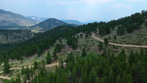 aerial view of a winding mountain road leading through green forests and rocky terrain, with distant peaks