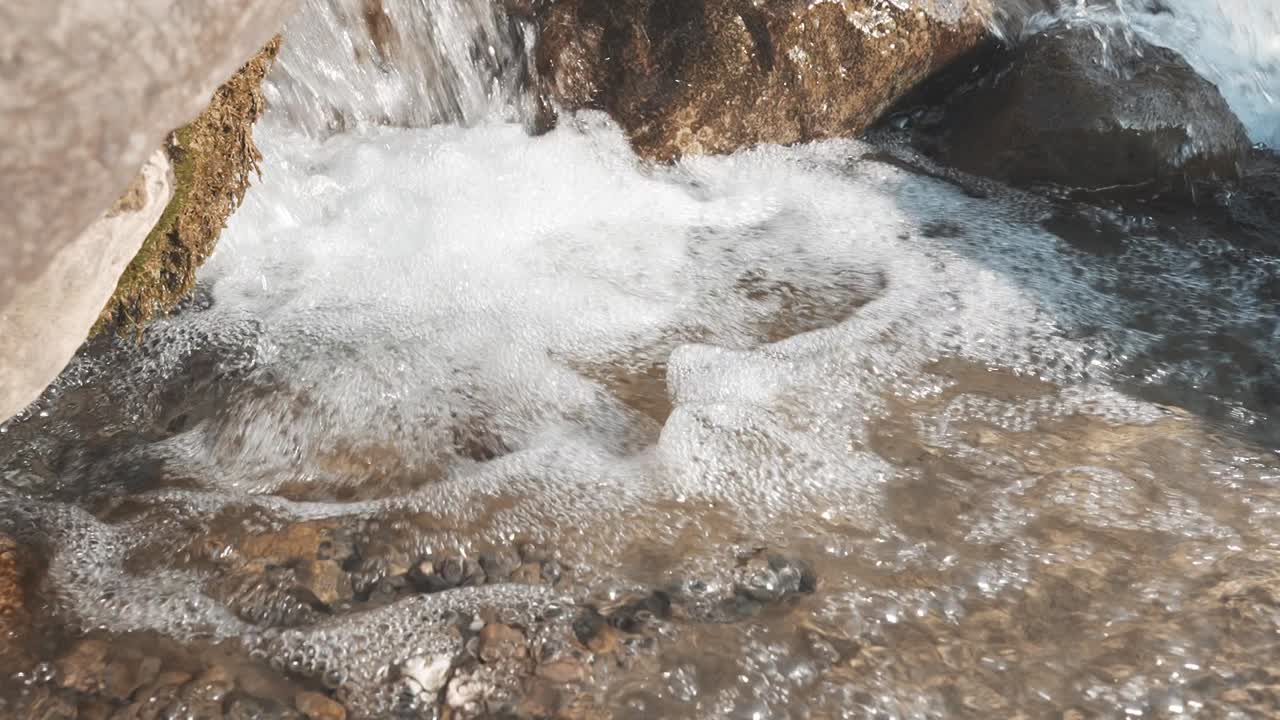 Close-up of water flowing over rocks in a mountain river near Walensee, Switzerland. The rushing water creates a gentle cascade, capturing the raw beauty of the Swiss Alps.