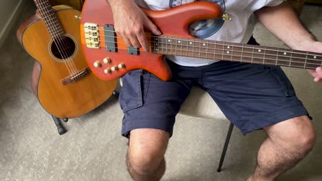 a mature man playing, practising bass guitar, sitting on a chair at home