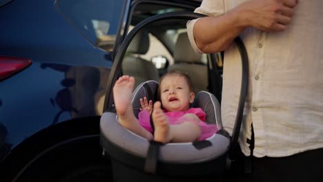 un bebé llorando en un asiento de coche mientras es sostenido por un padre
