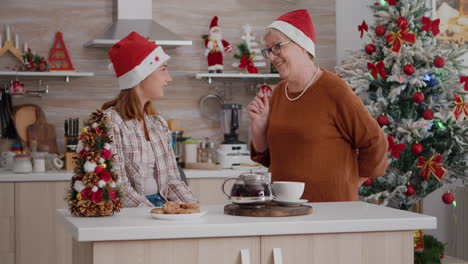 Grandmother-bringing-wrapper-present-gift-with-ribbon-on-it-to-granddaughter-enjoying-christmastime