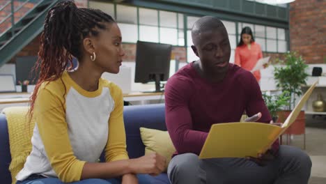 Happy-african-american-female-and-male-business-colleagues-reading-files-at-office