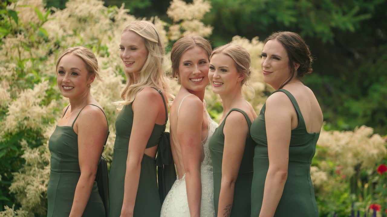 Bride and bridesmaids pose smiling laughing together in garden in slow motion