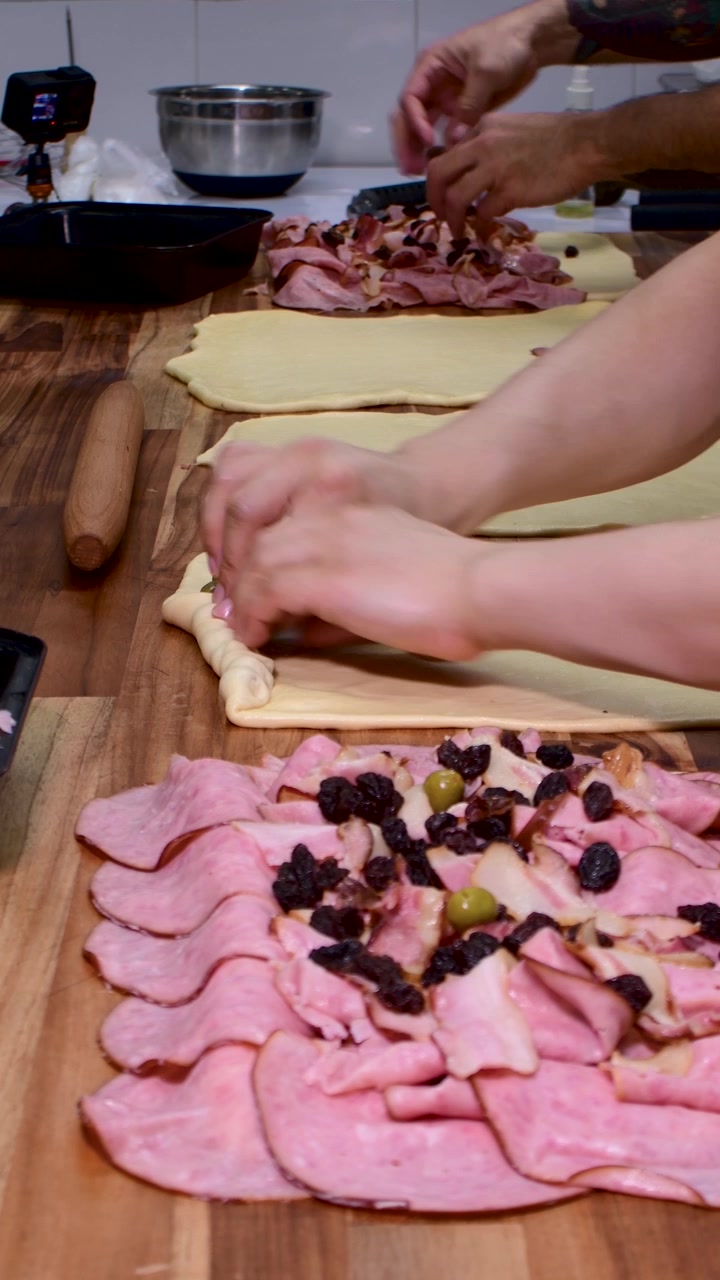 Due fornai stanno cucinando pan de jamón contemporaneamente su tavoli di legno.