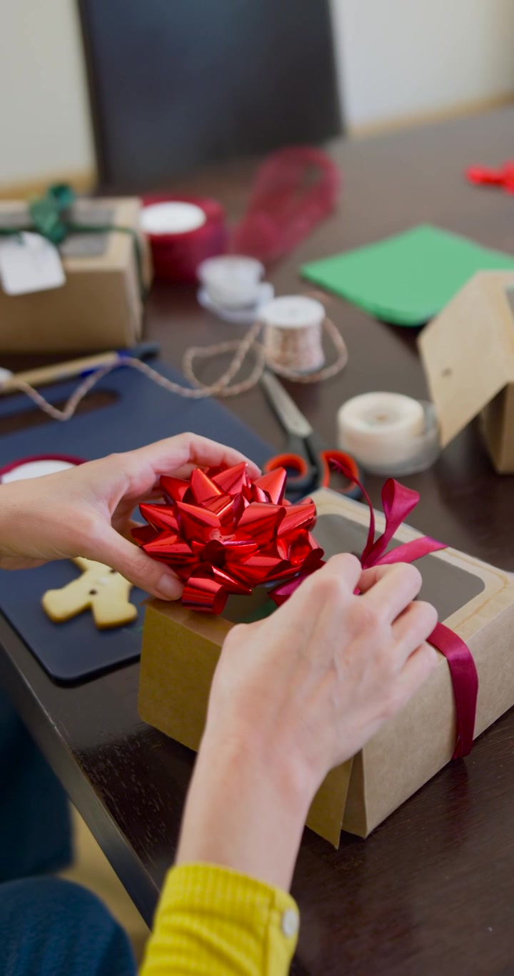 Video verticale: Donne che legano un nastro, una in giallo che posiziona un fiocco rosso su una scatola di cartone kraft a casa per Natale