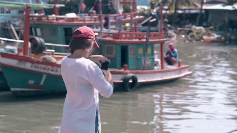 girl tourist shoots fishing boats on phone backside view