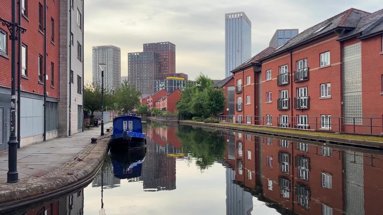 Manchesterkanalen med smalbåt, röda tegelhus och skyskrapor.