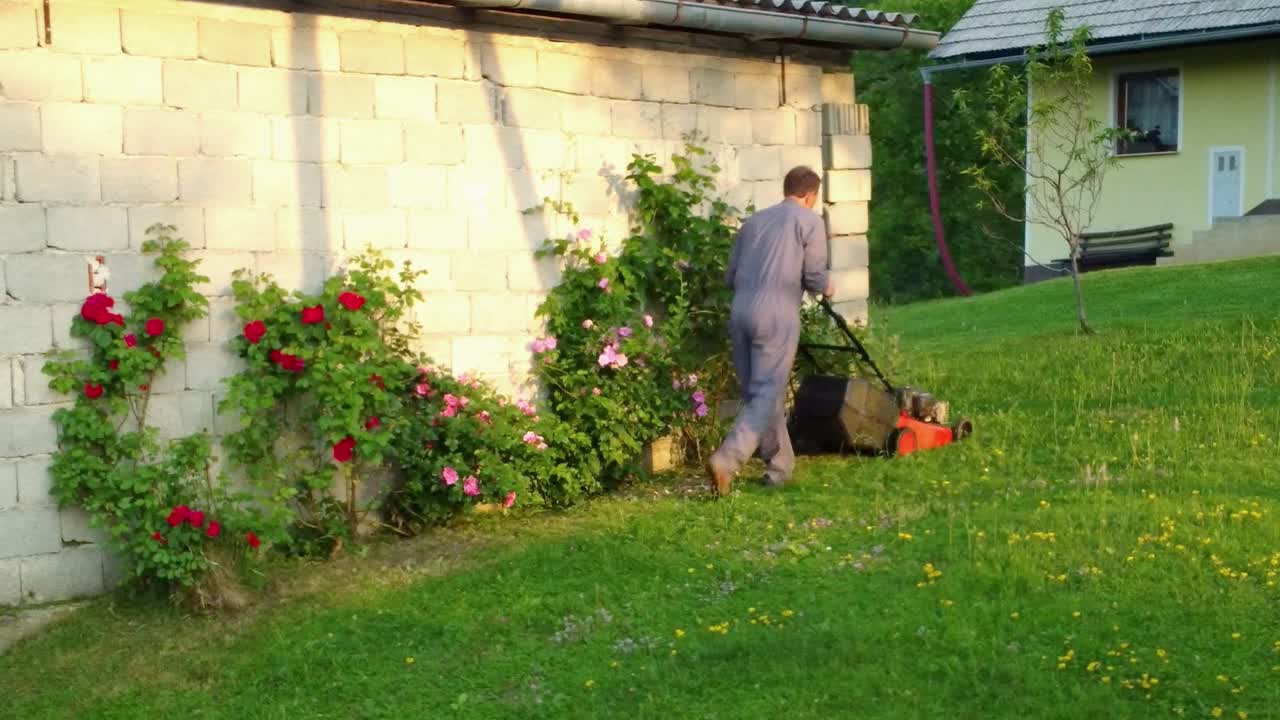 Man trimming his lawn around his garage with petrol rotary lawn mower machine