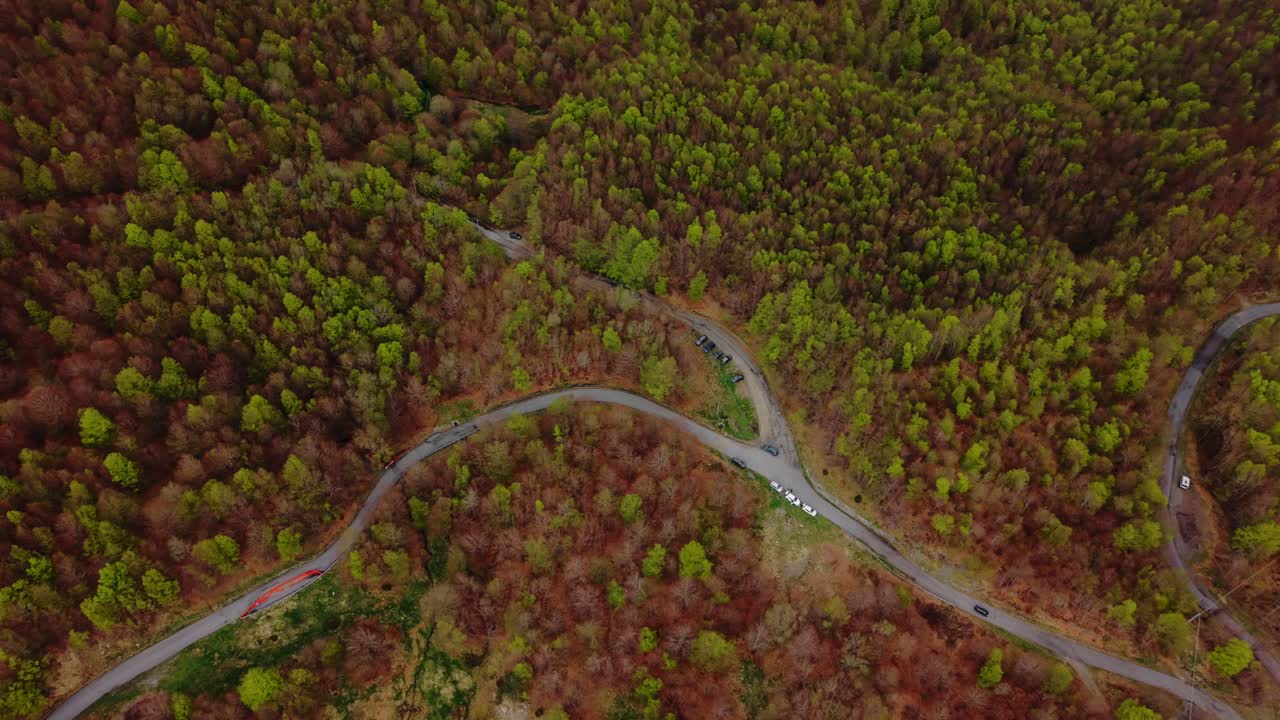 Winding mountain road through dense forest with old radar on summit, aerial view