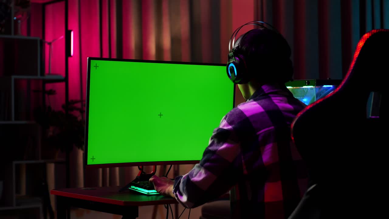 Giovane gamer asiatico entusiasta festeggia la vittoria mentre gioca a un videogioco al computer con schermo verde per mockup.