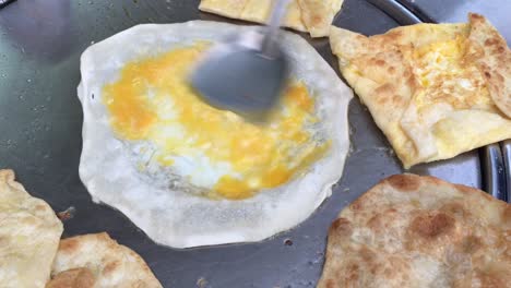 cocinar panqueques tailandeses exóticos, roti malaysian con diferentes rellenos en un mercado de tailandia. hacer rollo de roti de huevos en sartenes de metal calientes con aceite hervido. comida callejera de tailàndia. postre tailandés.