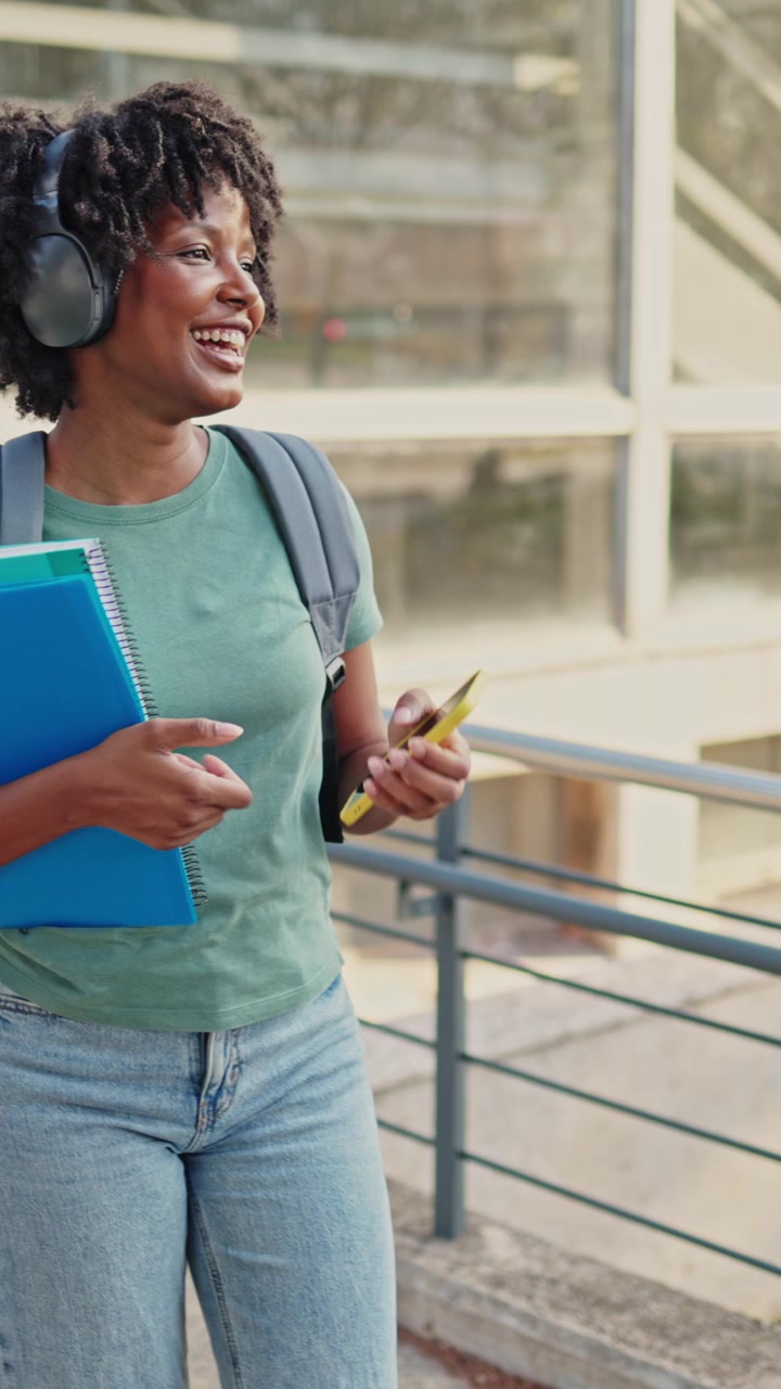 Happy African American Student with Headphones and Notebooks Using Smartphone
