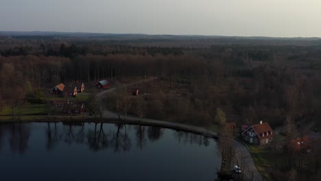 Drone-footage-of-a-car-driving-beside-a-lake-in-Sweden,-VÃ¤stersjÃ¶n-outside-Ã„ngelholm-in-SkÃ¥ne