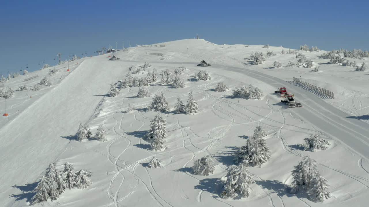 Battipista su una pista da sci innevata immacolata con alberi invernali e cielo azzurro limpido