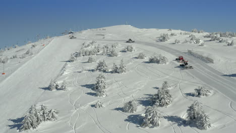 Snow Groomers on a Pristine Snowy Ski Slope with Winter Trees and Clear Blue Sky