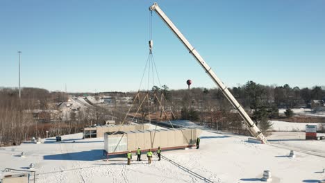 Aerial,-workers-installing-new-HVAC-unit-strapped-by-a-crane-onto-building-roof