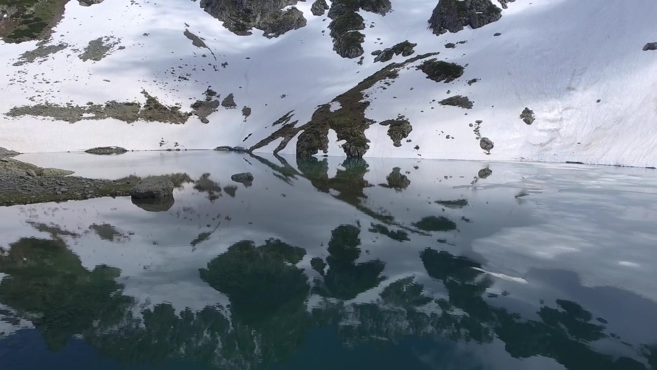 Delvist frossen alpinsø omgivet af snedækkede bjerge