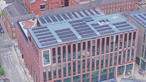 an aerial shot of a building with solar panels covering its rooftop. a construction site with cranes and workers can be seen nearby. the building is located in a city, surrounded by other buildings