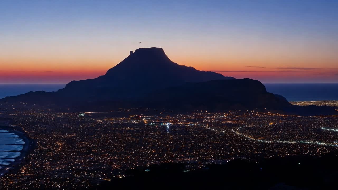 남아프리카 공화국 케이프타운의 라이온스 헤드 산과 대서양을 가로질러 해가 지는 동안 도시 불빛이 빛나고 있습니다.