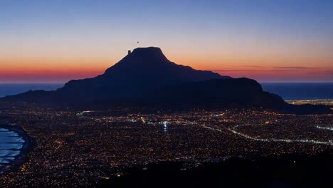 luces de la ciudad iluminando como el sol se pone sobre la montaña de cabeza de león y el océano atlántico en ciudad del cabo, sudáfrica