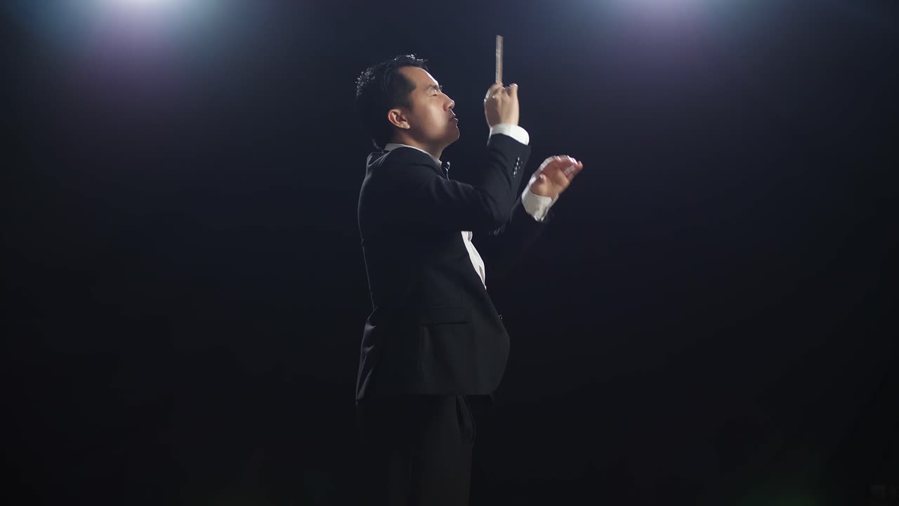Side View Of Asian Conductor Man Holding A Baton Closing His Eyes And Showing Gesture Quickly In The Black Studio