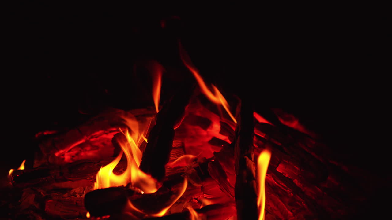 Burnt wood smoldering in the campfire. Beautiful red embers with small flames on. Close up. Black backdrop.